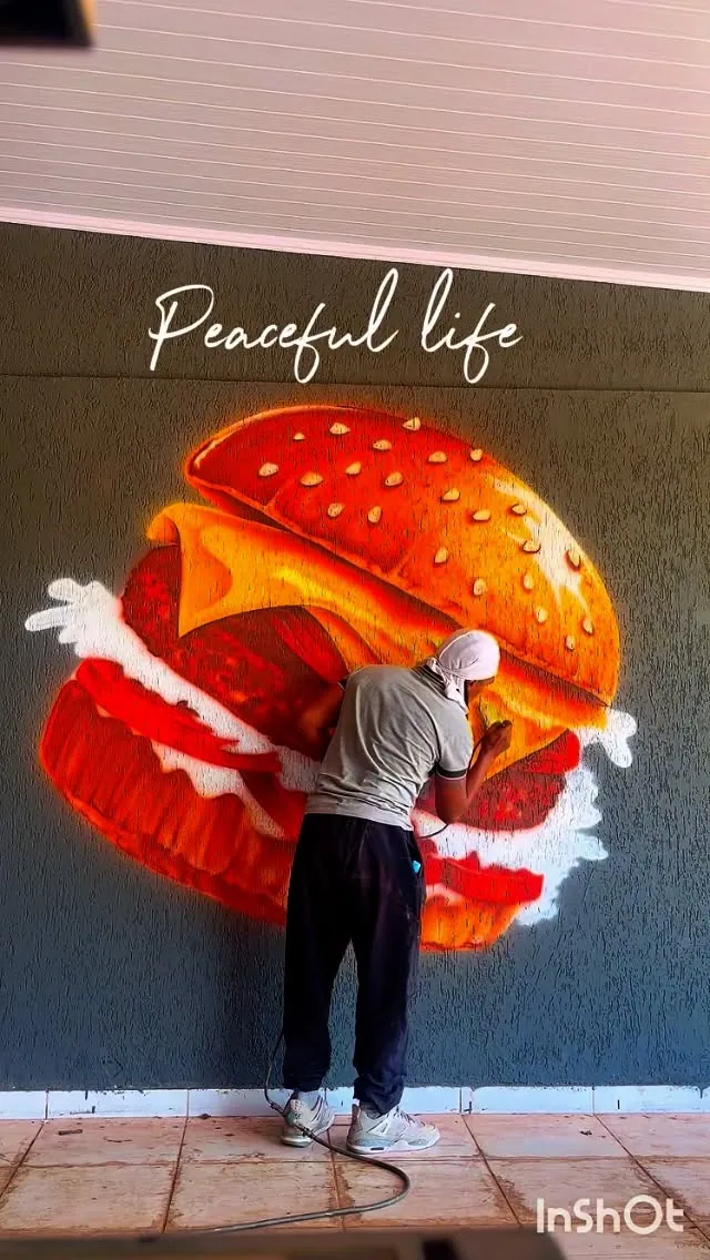 Artista ao lado do mural de hambúrguer, mostrando a escala real da obra