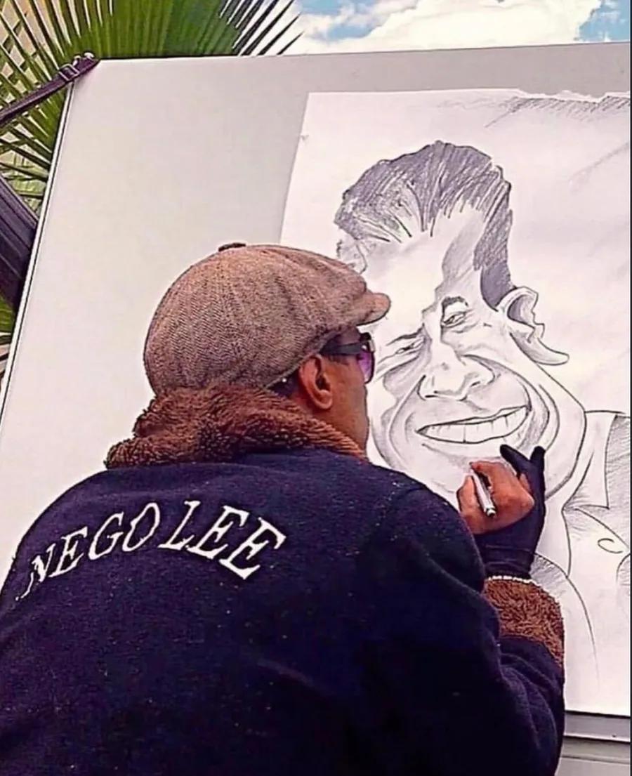 William Weber desenhando ao ar livre, vestindo jaqueta com a assinatura Nego Lee